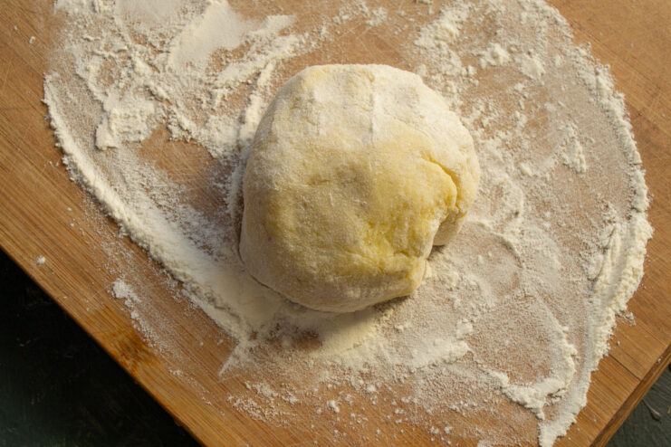 A hand mixing potato, egg, and flour in a bowl to form a soft gnocchi dough.