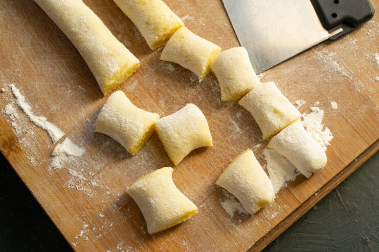 A long rope of gnocchi dough on a floured surface being cut into small, bite-sized pieces.