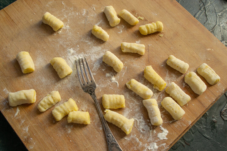 A piece of gnocchi dough being rolled over the tines of a fork to create characteristic ridges.