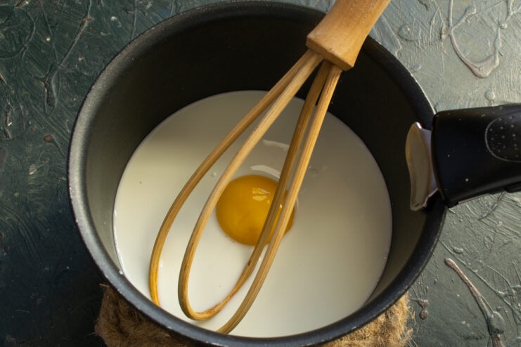 A saucepan containing milk and an egg yolk, the first step for making the cheese sauce.