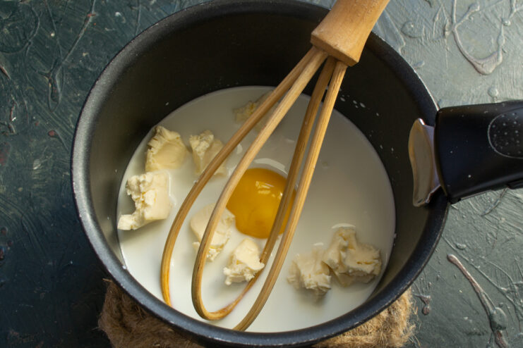 Soft processed cheese being added to the milk and egg mixture in a saucepan.