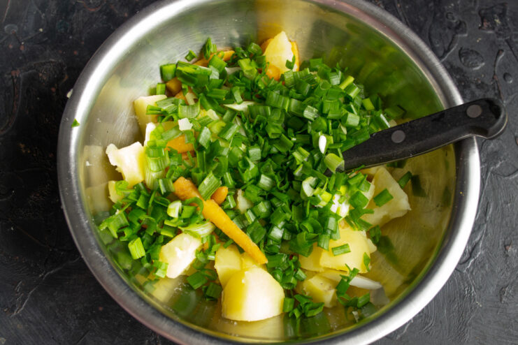 Adding chopped green onion tops to the potato and carrot salad base.