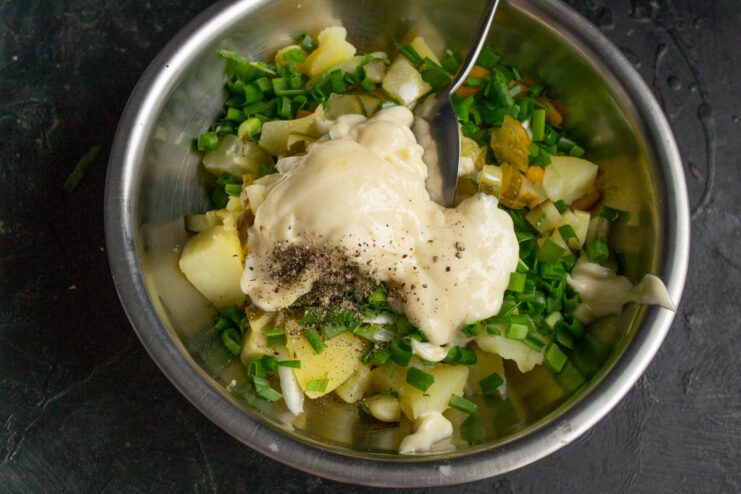 Adding a spoonful of homemade mayonnaise to the bowl of potato salad.