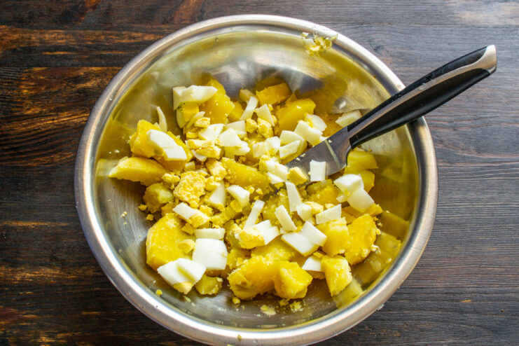 Step 2: Adding diced hard-boiled eggs to the salad Diced hard-boiled eggs being added to a bowl of potatoes.