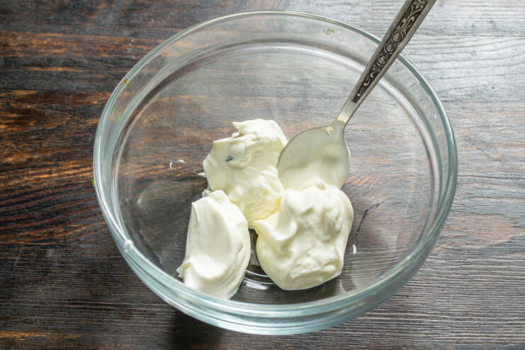 Making the creamy dressing for the potato salad Mixing cream cheese and thick sour cream in a white bowl to create a salad dressing base.