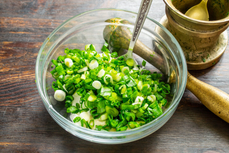 Adding fresh green onions to the salad dressing Adding finely chopped green onions to the creamy dressing in a white bowl.