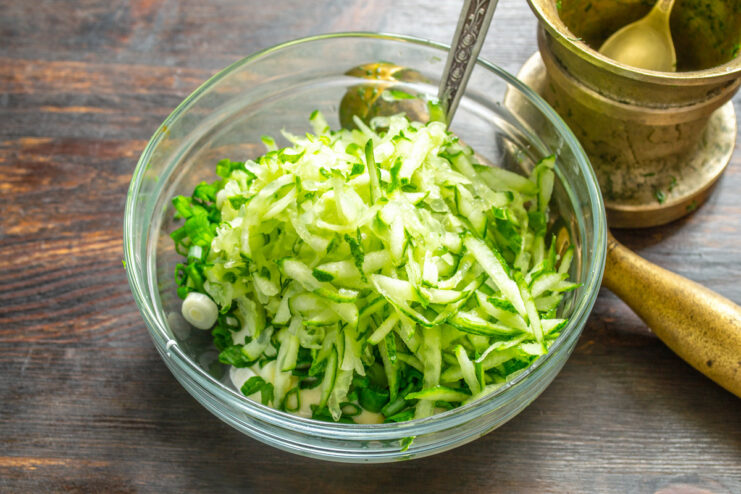 Grating fresh cucumber for the salad dressing A hand grating a fresh cucumber on a coarse box grater.