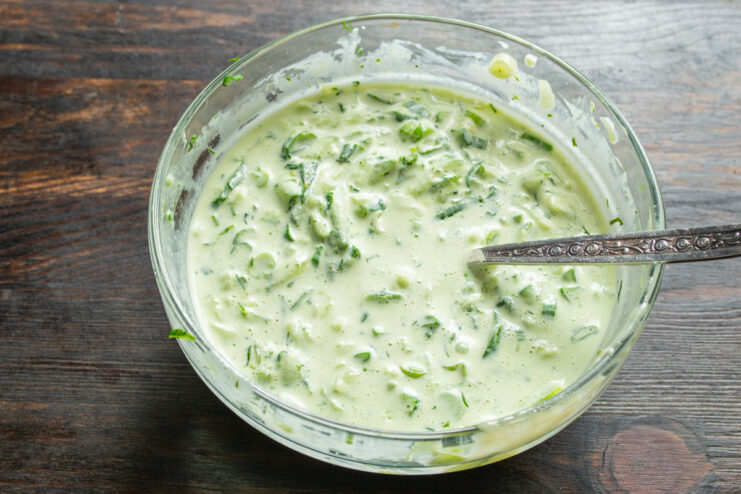 The final creamy green dressing for the potato salad A spoon mixing the finished creamy green dressing in a white bowl.