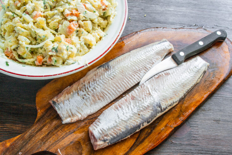 Pieces of herring fillet being placed on top of the finished potato salad.