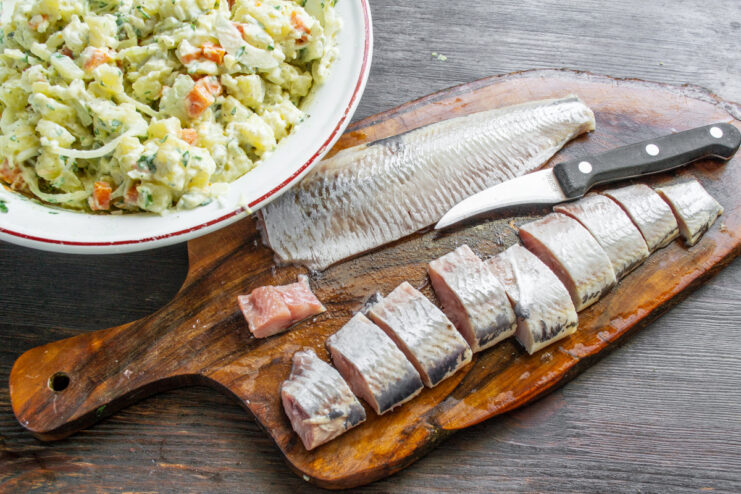 A herring fillet being cut into bite-sized pieces on a cutting board.