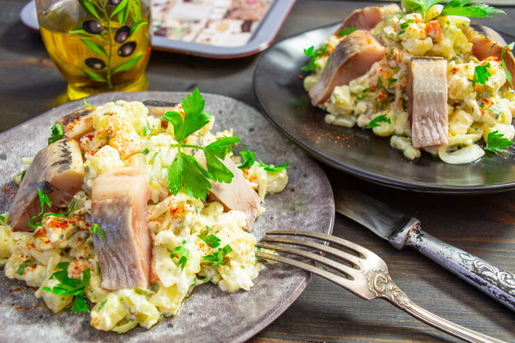 A bowl of finished potato salad with egg and herring, garnished with parsley.