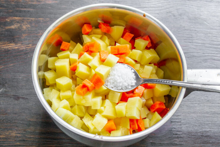 Diced raw potatoes and carrots on a cutting board, ready for boiling.