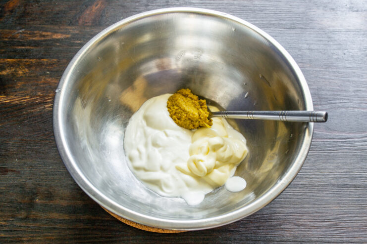 Preparing the Creamy Sour Cream and Dill Dressing Mixing sour cream, mayonnaise, and mustard in a glass bowl to make the dressing.
