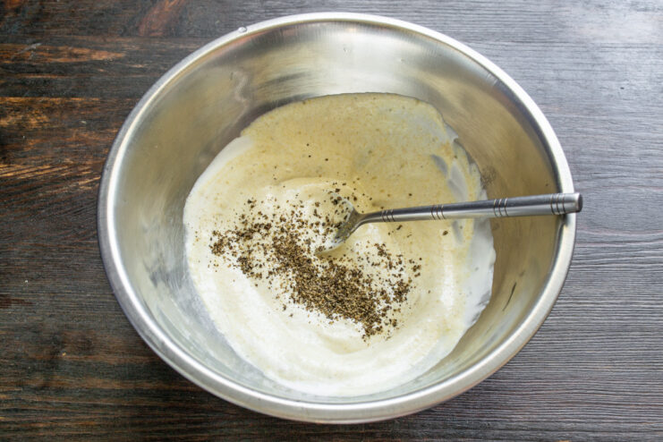 Seasoning the Dressing with Salt and Pepper Adding salt and freshly ground black pepper to the salad dressing in a bowl.