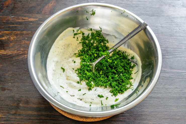 Adding Freshly Chopped Dill to the Dressing Freshly chopped dill being added to the sour cream dressing in a glass bowl.