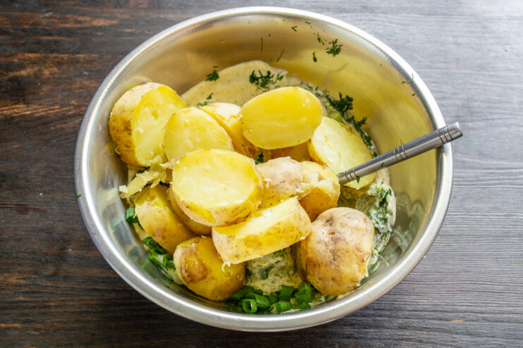 Slicing the Cooled Boiled Potatoes for the Salad Slicing cooled, boiled new potatoes on a cutting board.