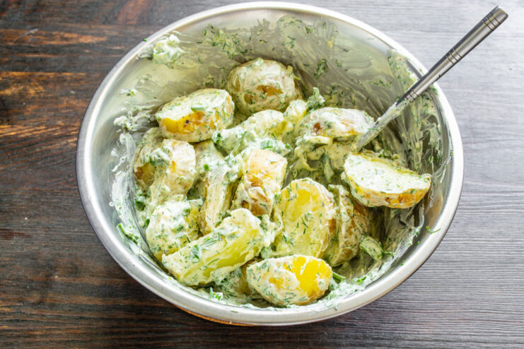 Gently Mixing the Potato Salad to Combine Gently tossing sliced potatoes with the creamy dill dressing in a large bowl.