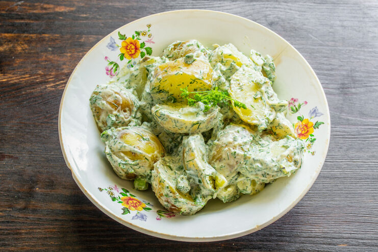 Serving the Potato Salad with Rye Bread and Cucumber A serving of potato salad with sour cream and dill on a plate, next to slices of rye bread and cucumber.