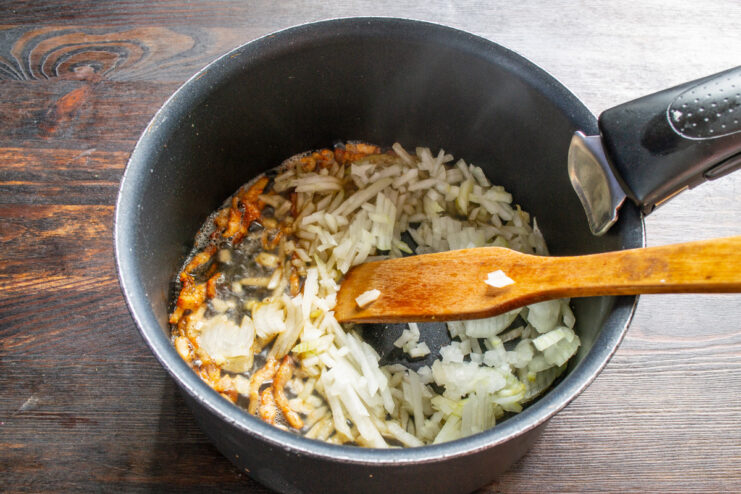 Sautéing onions and garlic with bacon for an aromatic soup foundation. Chopped onions and garlic being added to the pot with crispy bacon.