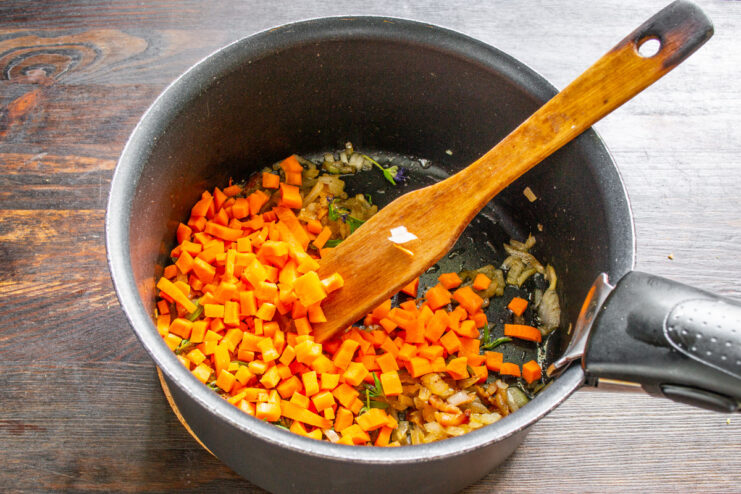 Adding diced carrots to the soup base for sweetness and color. Diced carrots being added to the pot with the other soup ingredients.