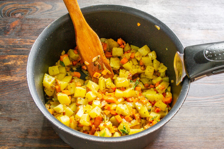 Adding diced potatoes, the star ingredient of the German soup. Diced potatoes being added to the pot with carrots, onions, and bacon.