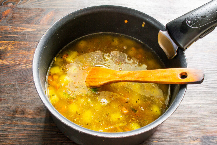 Pouring broth over the vegetables to create the soup. Pouring chicken broth into the pot over the sautéed vegetables.