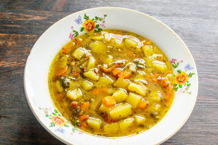 Serving the delicious, hot German potato soup. Ladling the finished German potato soup from the pot into a serving bowl.