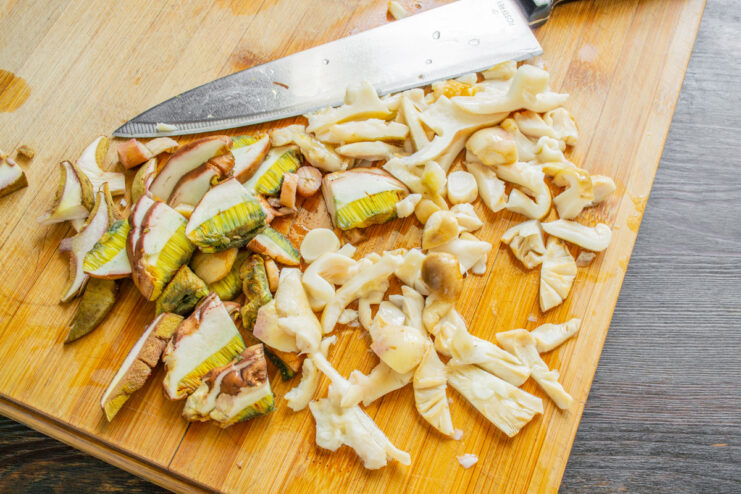 Slicing Cleaned Wild Mushrooms for Frying A pile of thinly sliced wild mushrooms on a cutting board, ready for cooking.