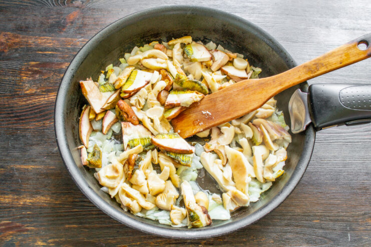 Adding Sliced Mushrooms to Sautéed Onions Sliced wild mushrooms being added to a pan with sautéed onions.