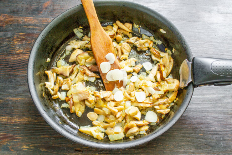 Seasoning Mushrooms with Garlic and Salt Sliced garlic and salt being added to mushrooms and onions cooking in a pan.