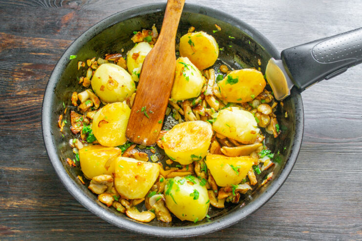 Combining Fried Potatoes with Cooked Mushrooms Golden-fried potatoes being mixed with cooked mushrooms and onions in a pan.