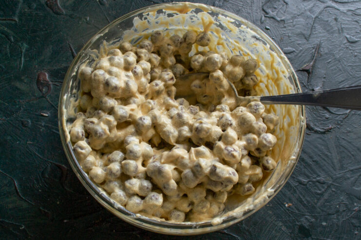 Combining the crunchy cereal with the creamy caramel base. A spatula mixing chocolate cereal balls with the caramel cream in a bowl.
