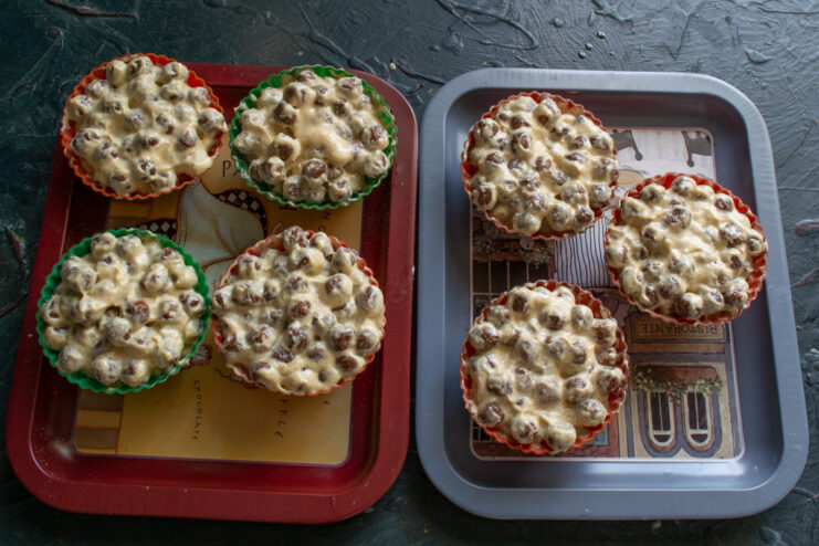 Portioning the mixture into muffin molds before chilling. A hand using a spoon to fill red silicone muffin molds with the chocolate cereal mixture.