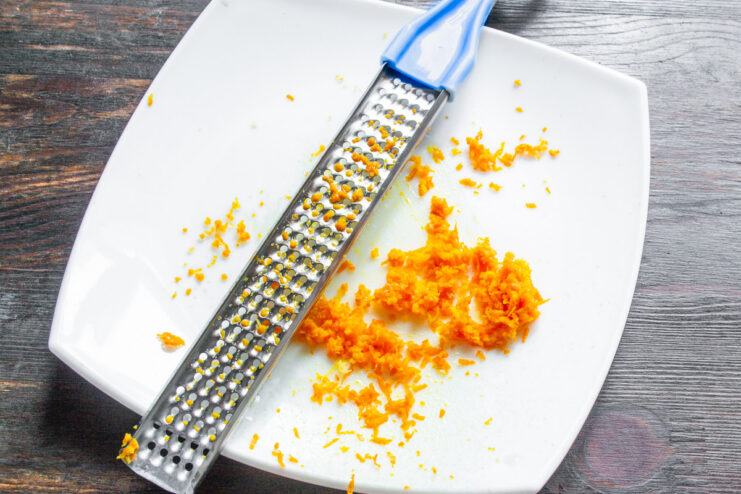 Adding Fresh Orange Zest for a Burst of Citrus Flavor A hand grating an orange on a fine metal grater to get fresh zest.