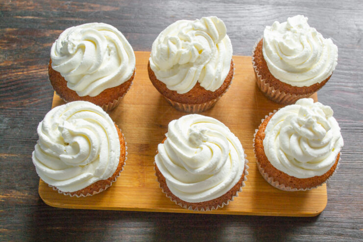 Frosting the Cooled Cupcakes with Homemade Whipped Cream A cupcake being decorated with swirls of whipped cream from a piping bag.