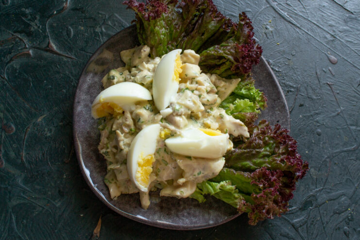 Garnishing the Salad with Hard-Boiled Egg Wedges A hard-boiled egg cut into quarters being placed on top of the chicken salad.