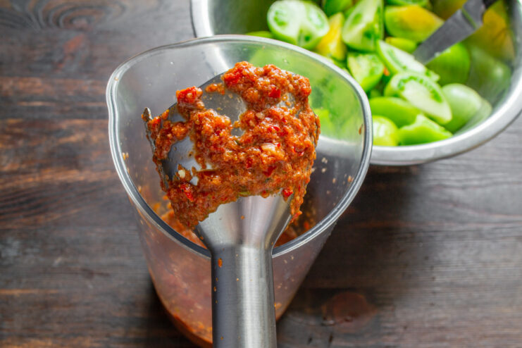 Blending the Kimchi Paste until Smooth An immersion blender pureeing red peppers and garlic into a smooth paste for kimchi.