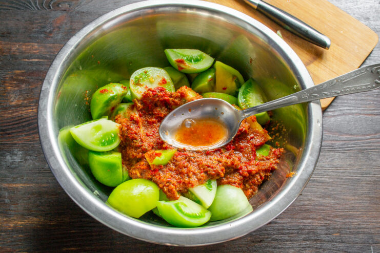 Combining Green Tomatoes with the Spicy Paste Spicy red kimchi paste being added to a bowl of chopped green tomatoes.