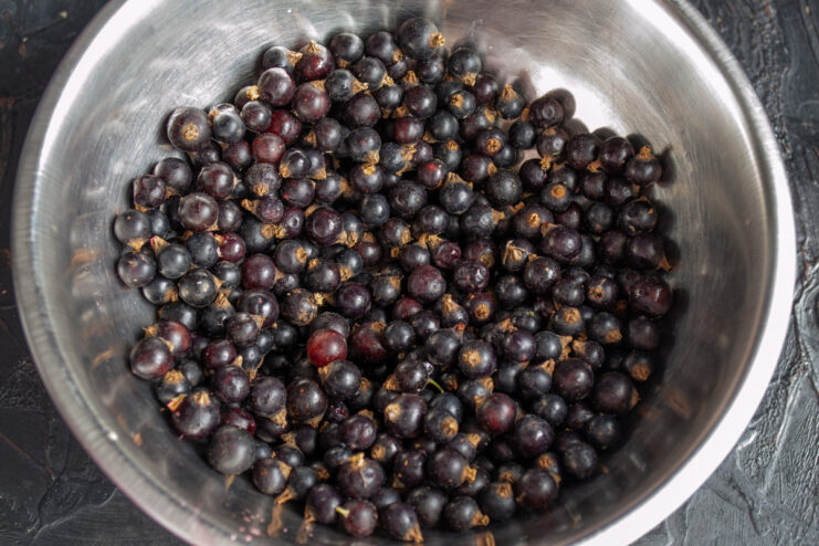 How to properly wash and prepare blackcurrants for the kisel recipe Fresh blackcurrants being rinsed in a white colander under a stream of water.