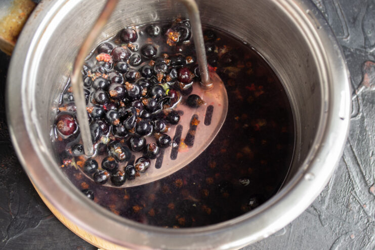 Mashing blackcurrants to extract juice without splashing Mashing blackcurrants with a potato masher in a saucepan to release their juice.