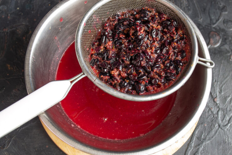 Straining blackcurrant juice to separate it from the pulp Straining the purple blackcurrant juice through a fine-mesh sieve into a bowl.