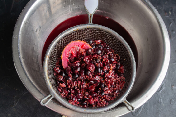 Straining the boiled blackcurrant pomace to get all the flavor Straining the cooked blackcurrant pomace through a sieve to extract the liquid.