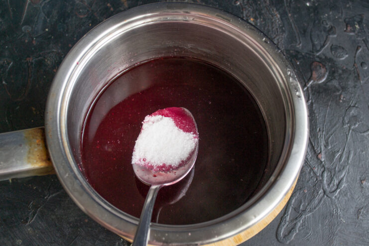 Adding sugar to the blackcurrant liquid before thickening Adding a spoonful of white sugar to the purple blackcurrant liquid in a saucepan.