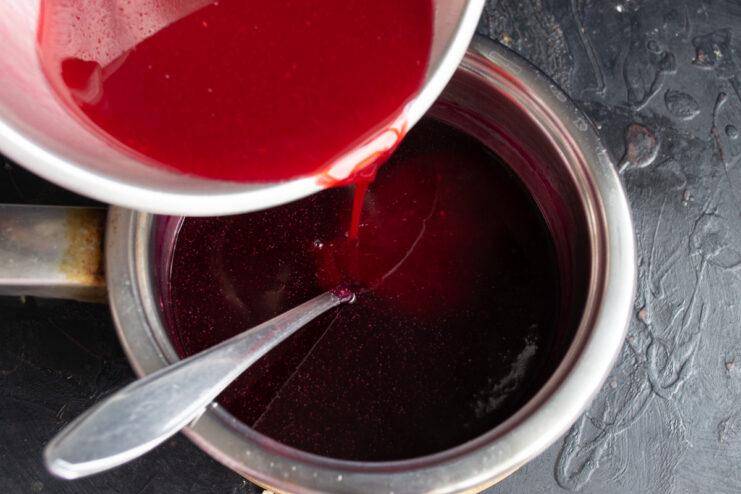 Adding fresh juice at the end to preserve vitamins and flavor Pouring fresh blackcurrant juice into the thickened kisel in the saucepan.