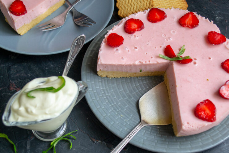 A slice of no-bake strawberry cake on a plate, decorated with fresh strawberries and mint.