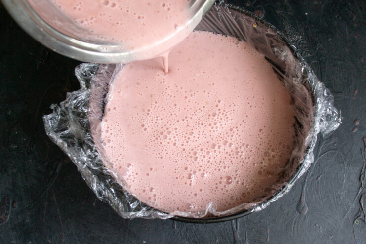 Step 10: Pouring the filling over the chilled cookie base. Pouring the pink strawberry and sour cream filling over the cookie crust in the pan.