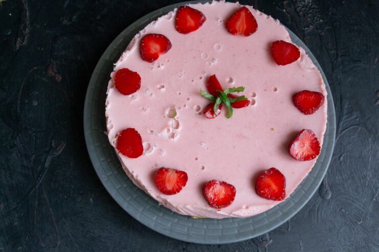Step 13: Decorating the cake with fresh strawberries and mint. The finished no-bake cake being decorated with fresh strawberry slices and mint.