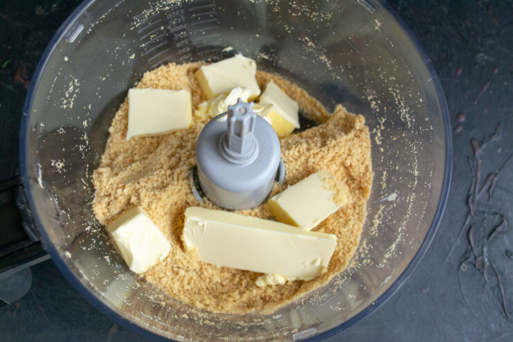 Step 2: Combining cookie crumbs with softened butter. Mixing cookie crumbs and butter in a blender using the pulse function.
