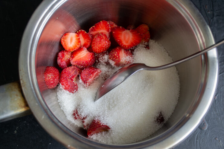 Step 6: Cooking strawberries with sugar in a saucepan. Fresh strawberries and granulated sugar in a saucepan, ready to be cooked down.