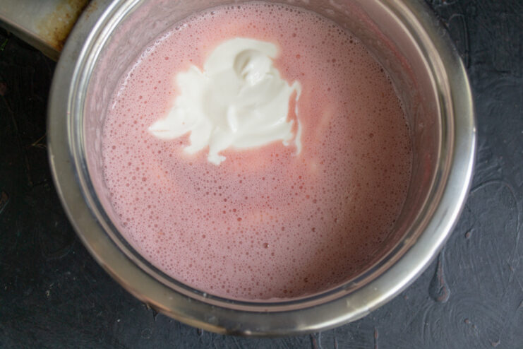 Step 9: Whisking sour cream into the strawberry mixture. Adding a spoonful of smetana (sour cream) to the strawberry and gelatin mixture.